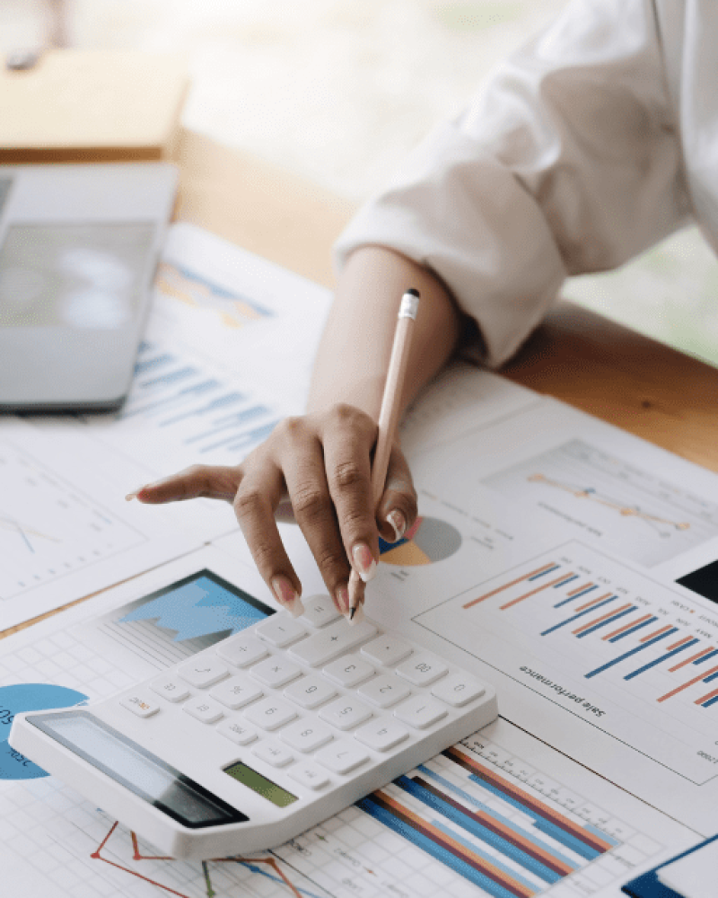 Close-up of a woman's hands doing calculations on a calculator of the finance documents spread on her desk and coffee cup in her other hand.